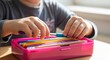 © alisya - Child's hands selecting a blue pen from a pink pencil box filled with colorful pencils