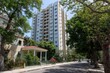© NANIK - Tall apartment building amidst lush trees old home street and cars on a sunny day