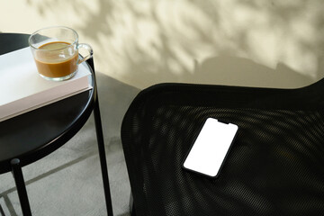Wall Mural - smartphone with a blank screen on mesh chair beside black table with book and a coffee cup