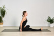 © TRAVELARIUM - Female adult in black outfit performs seated yoga pose on mat, in bright, minimalist room. Ambiance is calm and focused, highlighting flexibility and balance