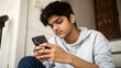 © Jo - Indian teenager in home clothes looking at mobile screen with focused expression