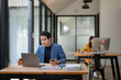 © Apichat - A man is sitting at a desk with a laptop and a cell phone