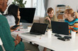 © SHOTPRIME STUDIO - Young adult woman coworkers socializing and working together in a modern workplace, representing Gen Z business colleagues collaborating on a project with laptops and casual attire.