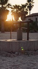 Wall Mural - aged water well nestled in verdant tropical foliage, bathed in golden sunset glow, casting warm oran
