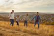 © Studio Romantic - Happy mother, father, son and daughter walking together in field, holding hands and looking cheerfully at each other, take stroll in nature during sunny autumn day. Family bonding concept