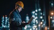 © Johannes - Young engineer in a helmet using a laptop and hands-free device during a night shift at an oil refinery, demonstrating commitment to safety and technology in the engineering industry