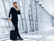 © Prostock-studio - Happy wealthy businessman standing in airport, talking on mobile phone with business partners or family and looking through the window, waiting for departure, travelling for work abroad, copy space