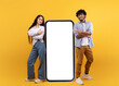 © Prostock-studio - Young indian spouses posing near huge smartphone with mockup, promoting mobile app or website, advertising your service or product over yellow studio background, free space