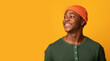 © Prostock-studio - Cheerful Young Black Guy In Hat Looking At Copy Space With Interest, Positive Millennial African American Man Thinking About Nice Offer Or Deal, Standing Over Yellow Studio Background, Panorama
