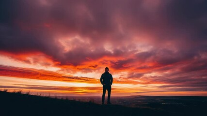 Wall Mural - person standing on hill with orange-red sunset clouds and expansive landscape
