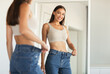 © Prostock-studio - Slimming Concept. Excited Slim Woman Wearing Jeans After Great Weight Loss Comparing Size Posing Standing Near Mirror At Home. Selective Focus, Cropped Shot