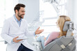 © Prostock-studio - Male dentist showing female patient jaw x-ray on digital tablet, dental clinic interior. Bearded man stomatologist having conversation with lady in dental chair, holding pad, side view, copy space