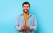 © Prostock-studio - Cheerful guy with smartphone looking at camera and smiling, texting in social media over blue studio background. Positive young man in casual chatting on phone, using new mobile application