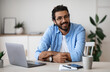 © Prostock-studio - Freelance Career. Handsome Indian Guy In Casual Wear Smiling At Camera While Sitting At Laptop Desk In Home Office, Young Cheerful Western Man Enjoying Working Remotely Online On Computer, Copy Space