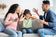 © Prostock-studio - Parental Quarrels. Arab Man And Woman Arguing In Front Of Their Child, Upset Little Girl Covering Ears With Hands Not To Listen Conflict, Stressed Female Kid Sitting Between Shouting Parents