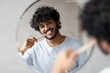 © Prostock-studio - Toothcare routine concept. Young indian guy cleaning teeth in the morning using toothbrush and toothpaste, standing near round mirror in bathroom