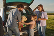 © Stockphotodirectors - Families gather for a delightful outdoor picnic, sharing smiles and laughter while a young girl plays with a stuffed animal beside an open vehicle in a serene landscape during sunset.
