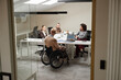 © Seventyfour - Diverse group of young adult professionals including Caucasian man with disability in wheelchair discussing business strategy around conference table in modern office