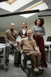 © Seventyfour - Diverse group of young adult professionals posing in modern office, including Caucasian man with disability in wheelchair