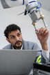 © Nassorn - Latino robotic development engineer working robot arm connection control at electronic futuristic science laboratory. Hispanic technician learning innovation machine in automated engineering academy.