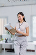 © MINAE - Smiling businesswoman wearing an ID card stands in her office, reviewing documents while a laptop and a neatly organized desk provide a modern backdrop to her professional environment