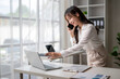 © Wasana - Asian businesswoman talking on phone and working on laptop in modern office
