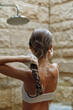 © SHOTPRIME STUDIO - woman washing hair in outdoor shower with stone wall background, wet brown hair, shampoo foam, summer wellness and care