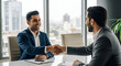 © Bboy - Happy young Indian business owner man shaking hands with male partner at meeting table, hiring new employee after interview,