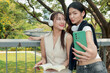 © Stella - Happy two beautiful Asian women use mobile phone to take a selfie photo together outdoor in park. Smiling close friends hold a book, spend time outside together in green garden. People in nature