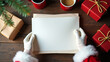 © APmit - Santa Claus's hands hold blank Christmas letter; festive gifts and warm drinks surround; cozy winter mood.