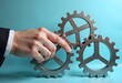 © Mahmuda - Hand Adjusting Interconnected Gears on Blue Background – Teamwork and Precision Concept
