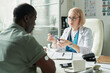 © pressmaster - Middle aged Caucasian female doctor explaining insulin pen to middle aged Black man with glucose monitor on arm during diabetes consultation in medical office setting