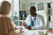 © pressmaster - Senior Caucasian woman with glucose monitor on arm consulting Black male doctor in medical office, doctor holding prescription bottle and discussing diabetes treatment options