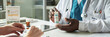 © pressmaster - Black male doctor explaining medication to middle aged Caucasian woman during diabetes consultation in medical office, hands holding prescription bottle near blood sugar chart and tablet