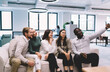 © BullRun - Young diverse professionals smiling while taking group selfie on office couch, creating lasting memory of team spirit, modern work culture and connection in casual workspace