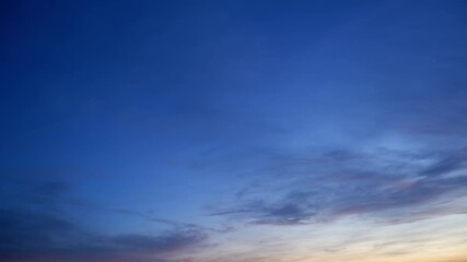 Wall Mural - a calm sunrise sky timelapse with soft gray and pink clouds gently drifting over a fading deep blue 