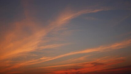 Wall Mural - a sunrise sky timelapse with soft orange and peach clouds gracefully stretching across a calm blue b