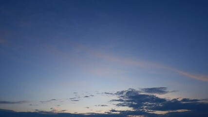 Wall Mural - A sunset sky timelapse showcasing vivid pink and orange clouds streaking across a deep purple-blue backdrop, with dark clouds below adding contrast, evoking a peaceful and dramatic evening scene. 
