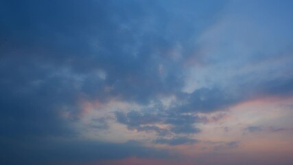 Wall Mural - a moody sunset sky timelapse featuring dark, dense clouds softly illuminated by warm orange and pink
