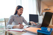 © Leo Lintang - Indonesian southeast asian businesswoman working with paperwork and a laptop on the table inside the hybrid workplace. Business concept. Remote working from home