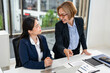 © Fahng - Two business women sit at desk discuss project details, diverse female colleagues met in office, share opinion, working on collaborative task, sales manager makes commercial offer to company client.