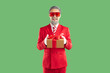 © Studio Romantic - Portrait of man in festive costume giving you Christmas present. Happy bearded man wearing red suit and funny party glasses standing isolated on green background, holding gift box and smiling