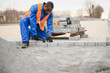 © Serhii - African american master in gloves lays paving stones in layers. Garden brick pathway paving by professional paver worker. Laying gray concrete paving slabs in house courtyard on sand foundation base