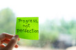 © Arianne - Hand holding sticky note with progress not perfection reminder
