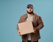 © VISTA by Westend61 - Young man holding a cardboard box in a studio portrait with a blue background