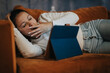 © qunica.com - A woman relaxes on a comfortable sofa, engaging with content on a tablet. Her casual attire and peaceful demeanor suggest leisure and a cozy home environment.