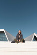 © VISTA by Westend61 - Woman sitting on steps outdoors in sunlight with modern architecture