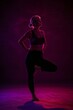 © Muhammad - Woman in tree pose yoga position silhouetted against pink and purple lighting in a studio setting