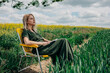© VISTA by Westend61 - Woman sitting on a yellow folding chair in a field of green wheat and yellow rapeseed, reading a book and enjoying the peaceful rural landscape