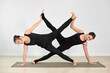 © TRAVELARIUM - Two adult women in black athletic wear perform partner yoga on mats, showcasing balance and teamwork. Minimalist studios neutral tones emphasize their dynamic pose. Scene conveys harmony and focus